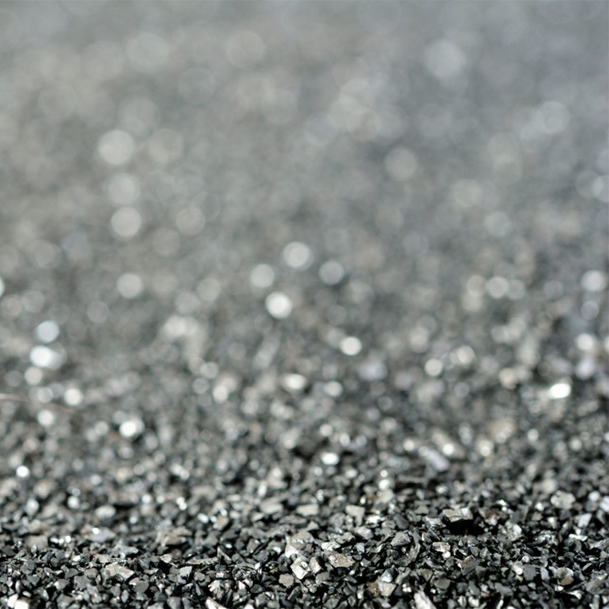 A granular, shiny black substance lies scattered, reflecting light, creating a twinkling effect in a soft-focus background, suggesting a processed mineral texture.