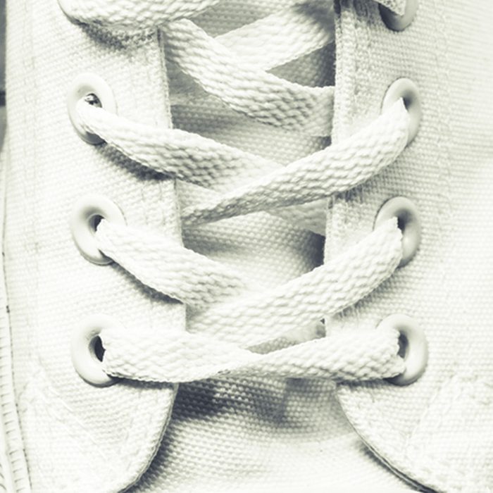 A white sneaker sits still, its laces crisscrossed through metal eyelets, showcasing the texture of the canvas in a close-up view.
