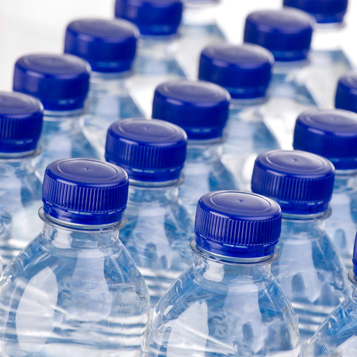 Rows of clear plastic water bottles with blue caps are arranged closely together, showcasing the transparent liquid inside each container.