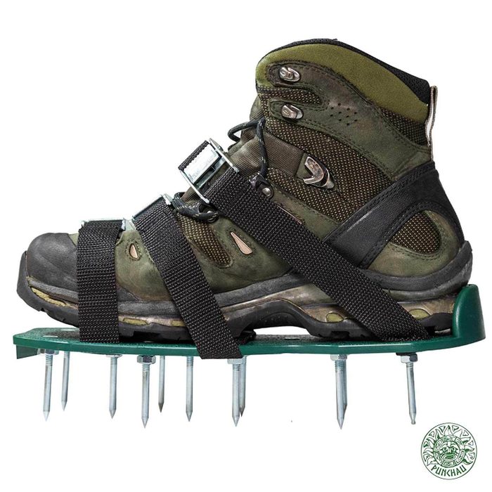 A rugged hiking boot is equipped with metal spikes attached to a green platform, designed to enhance traction on snow or ice.