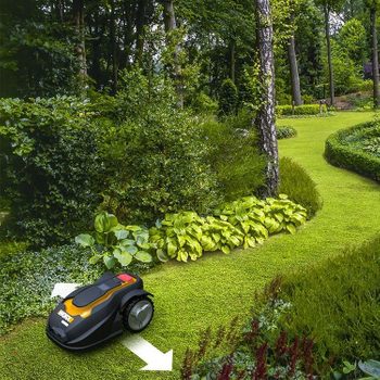 A robotic lawn mower moves across a green lawn, navigating around bushes and trees in a well-maintained garden.