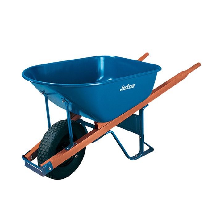 A blue wheelbarrow with wooden handles rests on a tire, designed for transporting materials in gardens or construction sites.