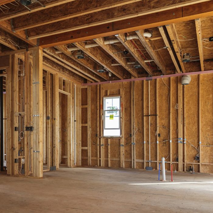 Unfinished interior space featuring wooden framing, bare walls, and a single window. A few construction markers stand on the floor. Light enters through the window.
