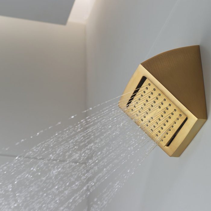 A golden showerhead releases streams of water, illuminating a modern, minimalist bathroom with soft lighting and muted colors.