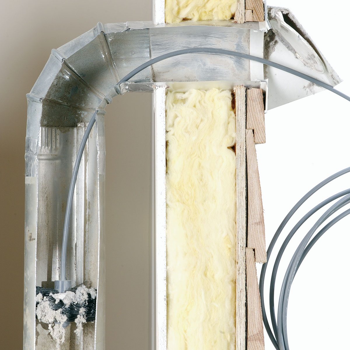 A cross-section of a wall shows insulation material and metal ducting, with flexible tubing running through. The background is a plain white surface.