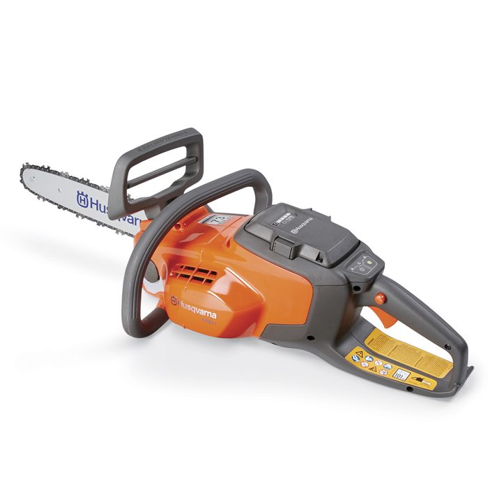 A chainsaw rests on a flat surface, ready for use. Its sharp blade is visible, with an orange and black ergonomic design featuring safety instructions nearby.