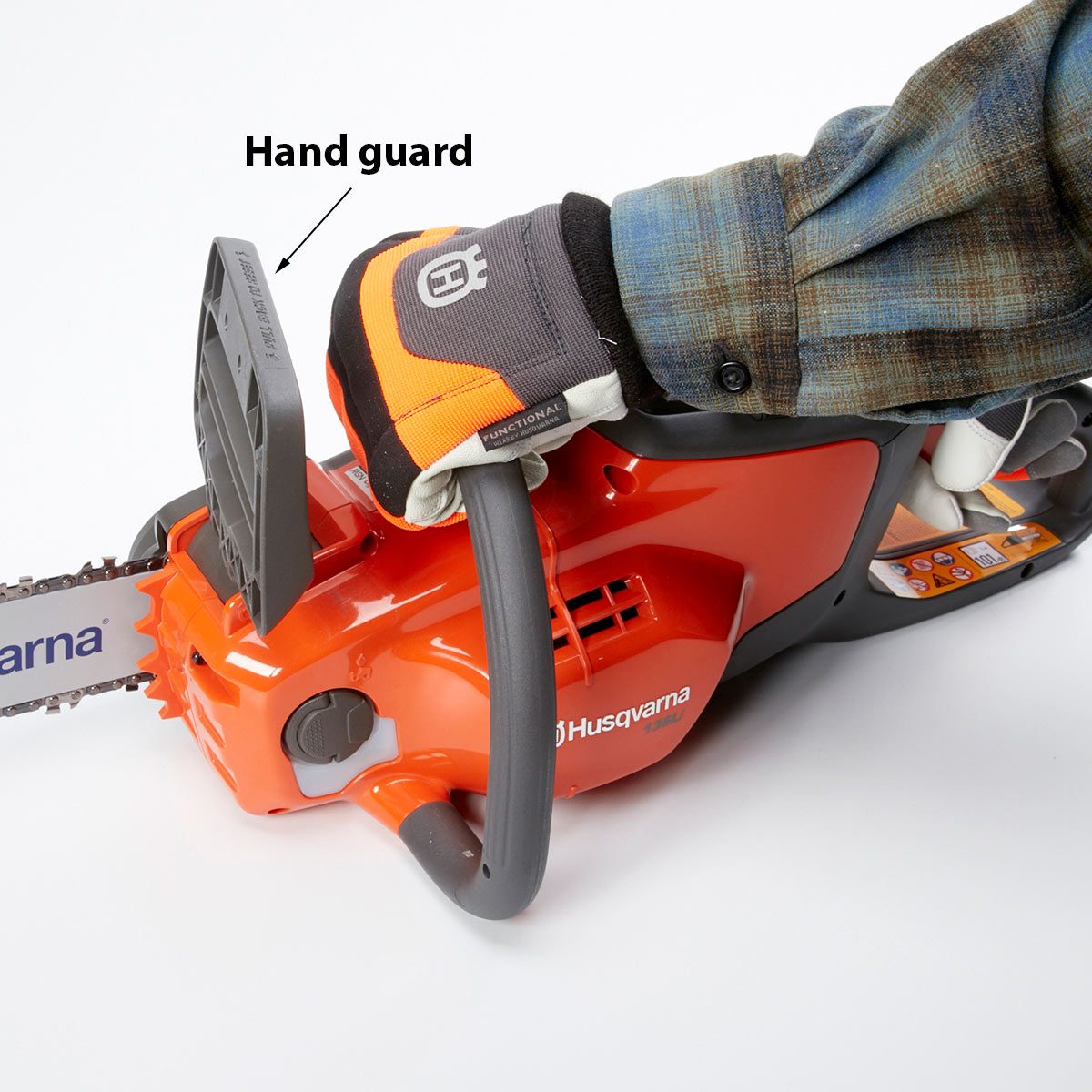 A chainsaw rests on a surface, while a gloved hand grips its hand guard, demonstrating proper handling. The environment is plain and neutral.