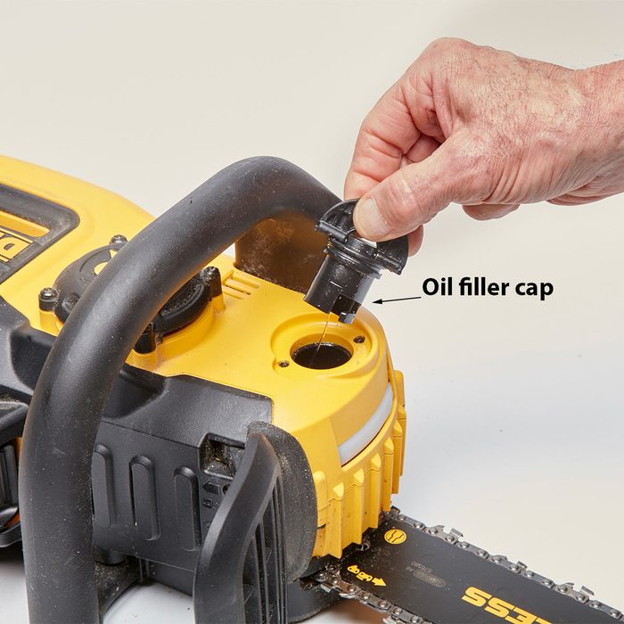 A person is removing the oil filler cap from a chainsaw, preparing to add oil. The chainsaw has a yellow and black design.