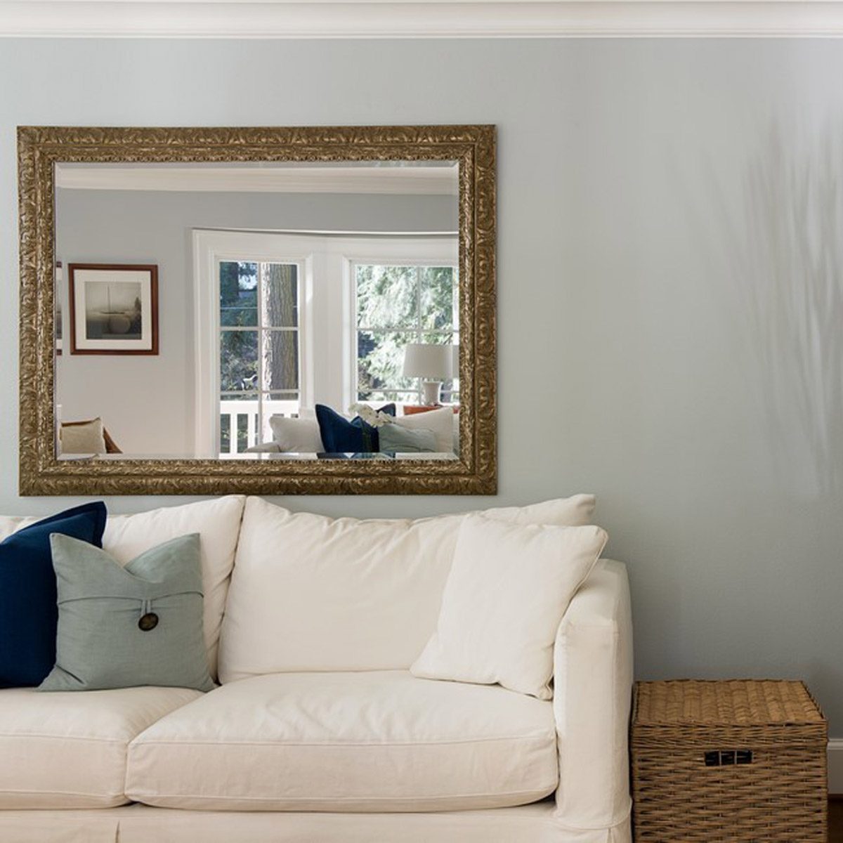 A decorative mirror reflects a cozy living space, while a white sofa with pillows sits nearby, accompanied by a woven storage box in the corner.