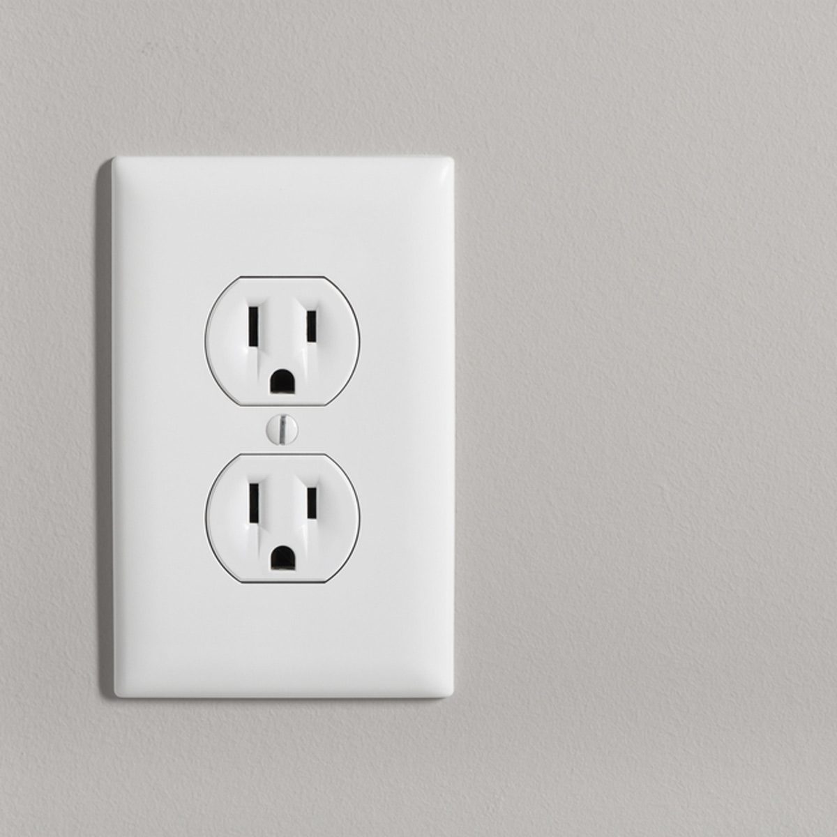 A white electrical outlet with two sockets is affixed to a plain gray wall. It is inactive and ready for use.
