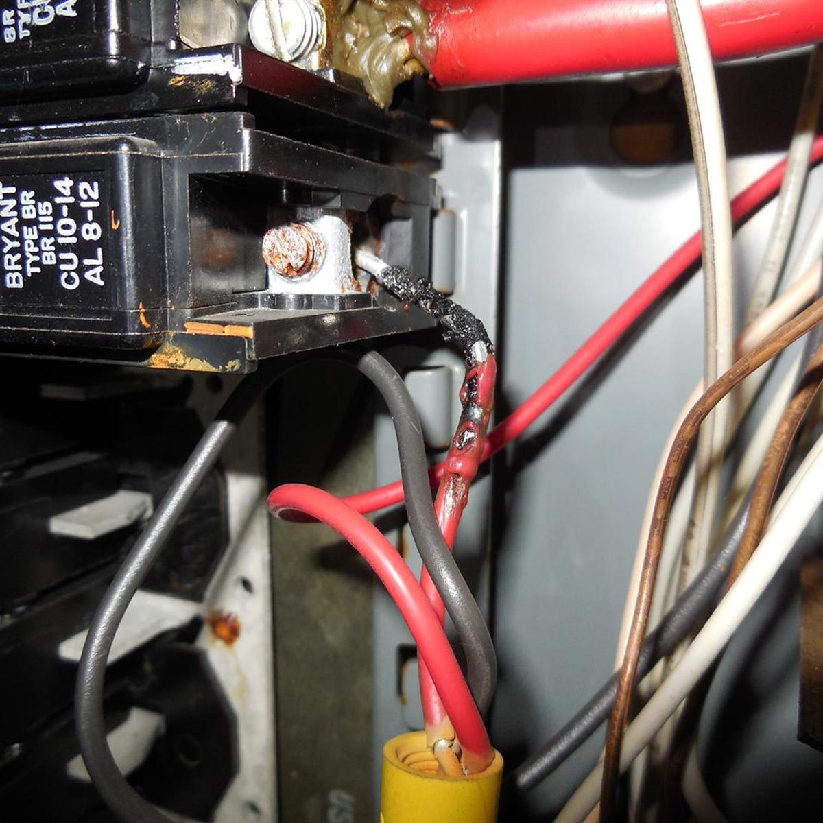 A damaged electrical wire connects to a circuit breaker, exhibiting frayed insulation and corrosion, within a cluttered electrical panel.
