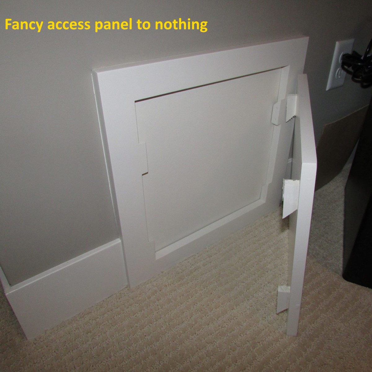A white access panel is ajar, revealing an empty space behind it, set against a gray wall and soft, beige flooring.