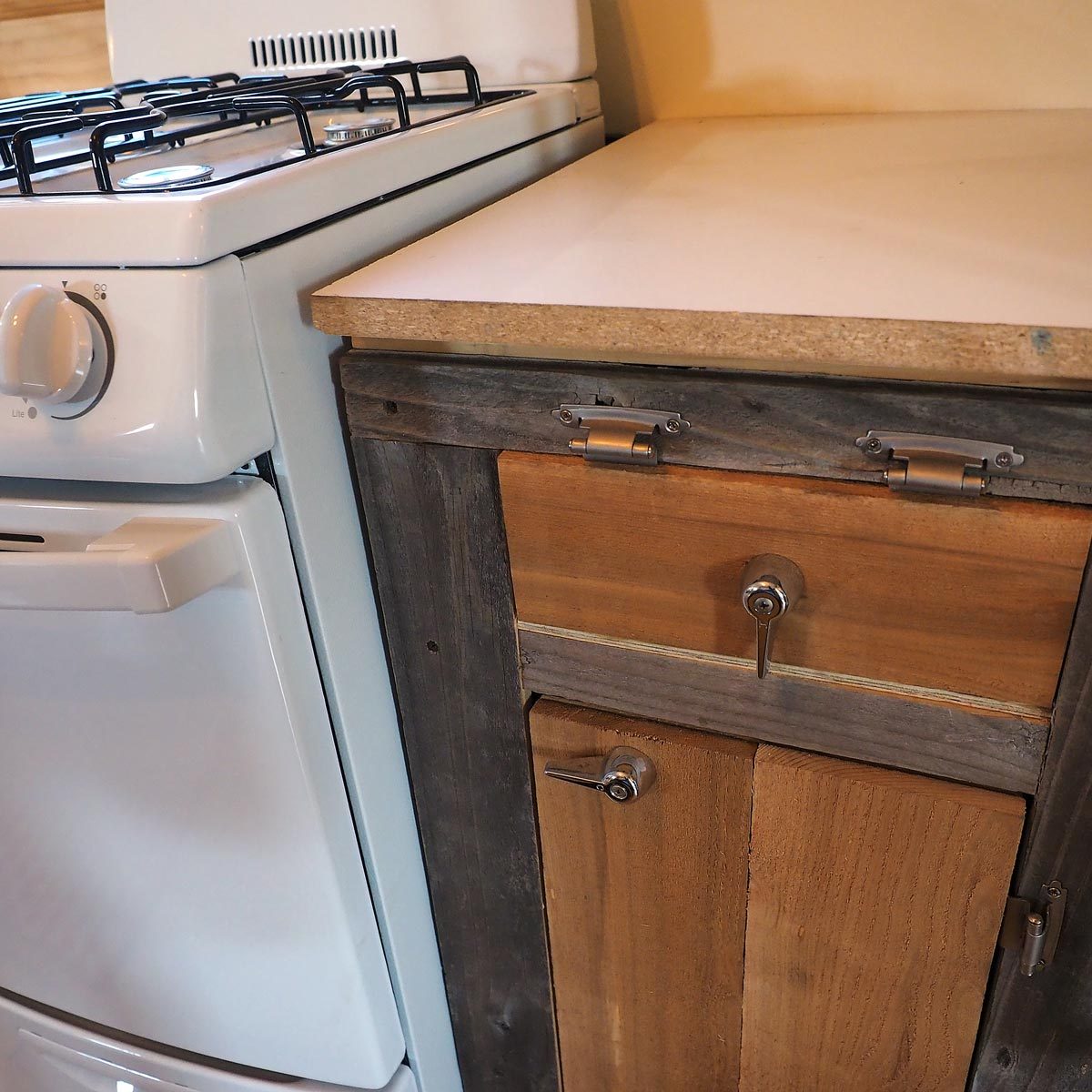 A white gas stove is positioned next to a rustic wooden cabinet with metal knobs, set on a light-colored countertop in a cozy kitchen.