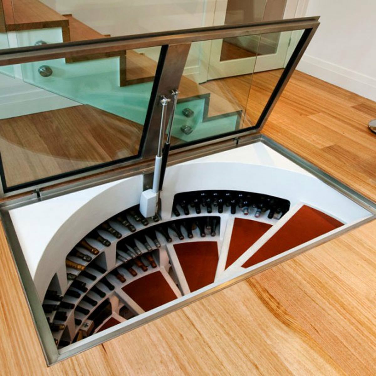 A glass hatch reveals a spiral wine storage cellar beneath a wooden floor, displaying numerous wine bottles organized in a circular arrangement.