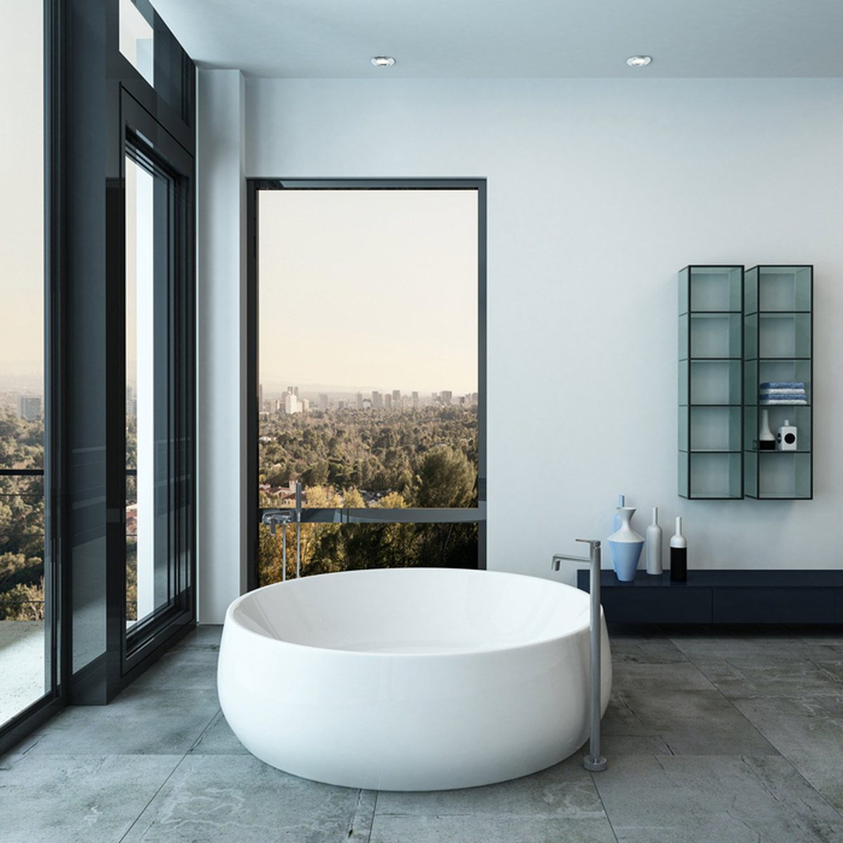 A modern, freestanding bathtub sits on stone tiles, overlooking a cityscape through large windows, with minimalistic decor including shelves and decorative bottles nearby.