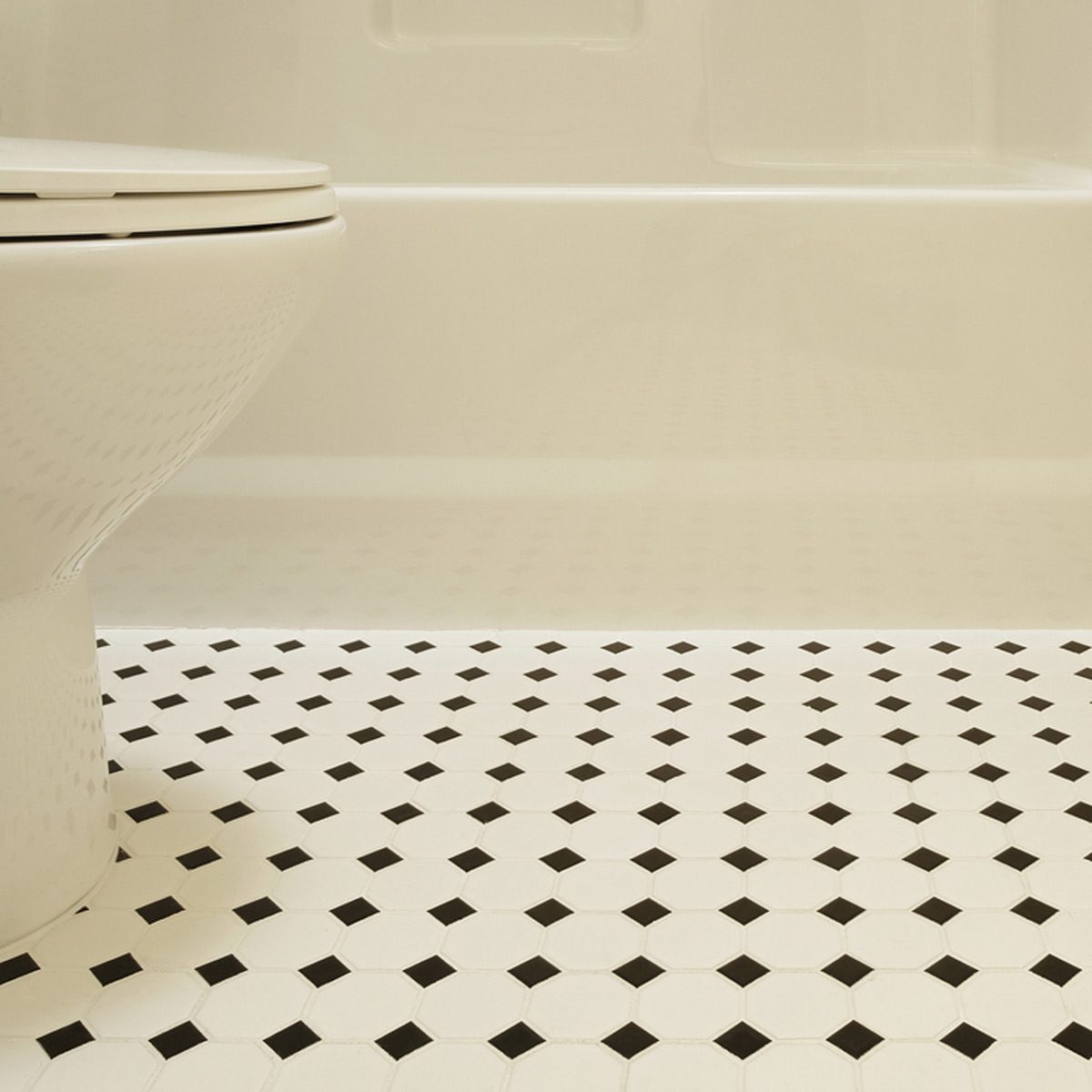 A white toilet is positioned next to a patterned floor of black and white tiles, within a clean, light-colored bathroom environment.