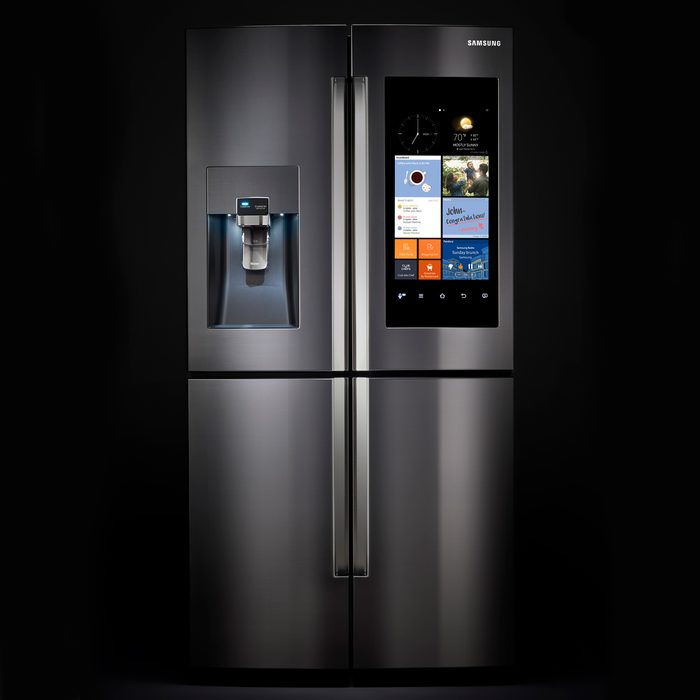 A sleek black refrigerator features a water dispenser and a digital screen displaying apps, weather, and information, set against a dark background.