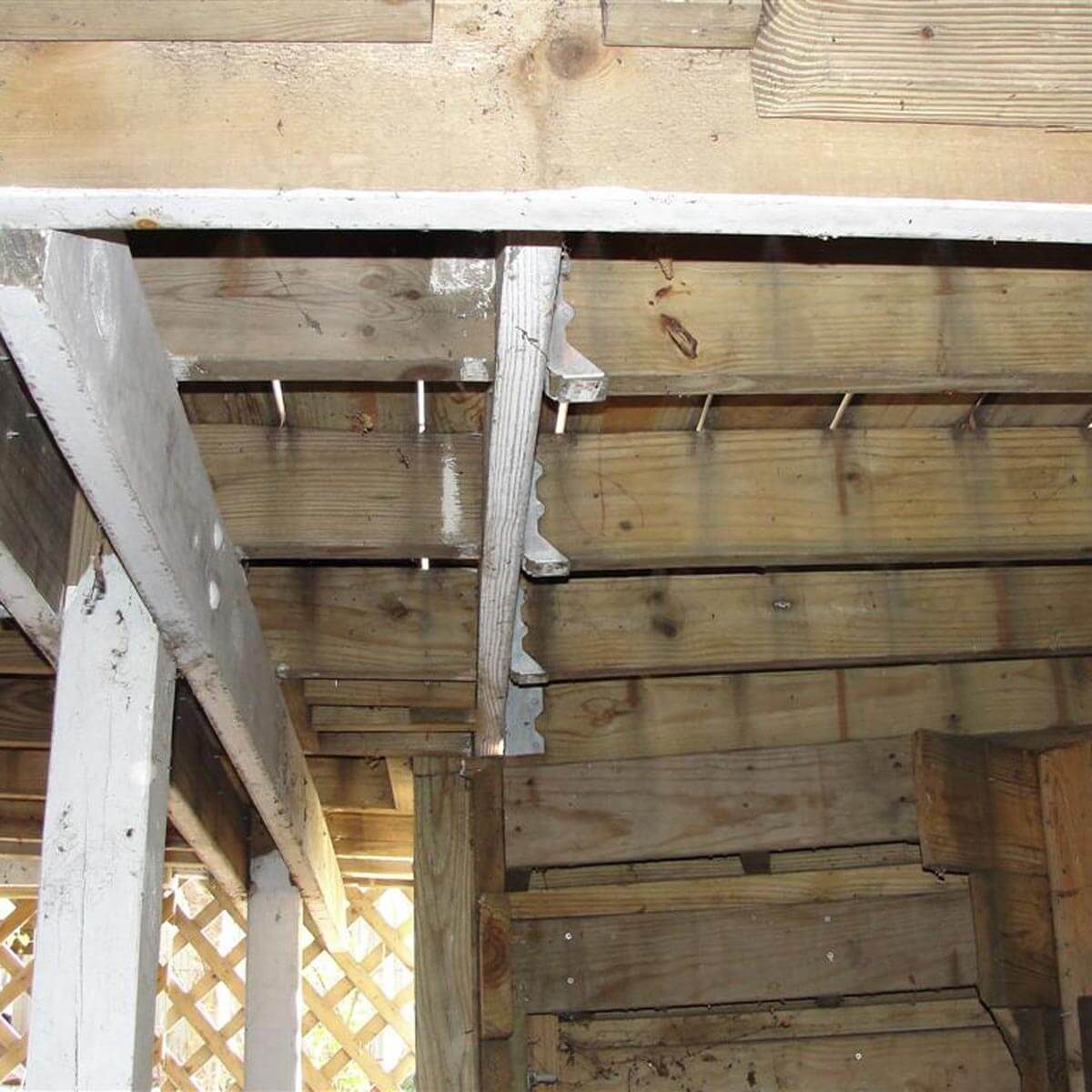 Wooden beams and metal supports create a framework, revealing an unfinished, rustic interior space with exposed structure and natural light filtering through gaps.