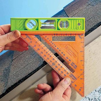 A green level and orange square are held against a roof edge, ensuring proper alignment in a construction context. Bright blue sky is visible above.