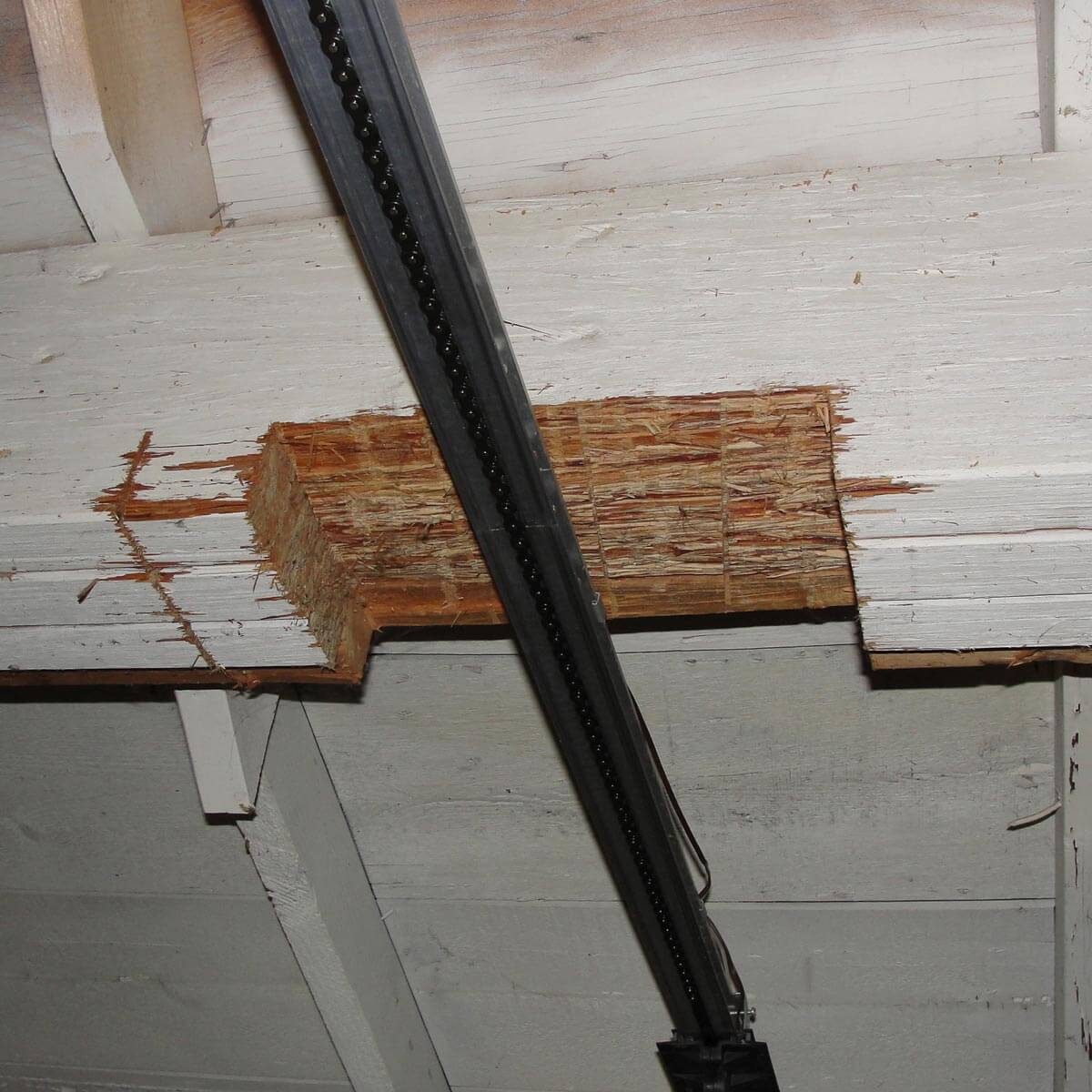 A wooden beam has a significant section removed, exposing the inner structure, while a metal rail runs parallel above in a dimly lit environment.