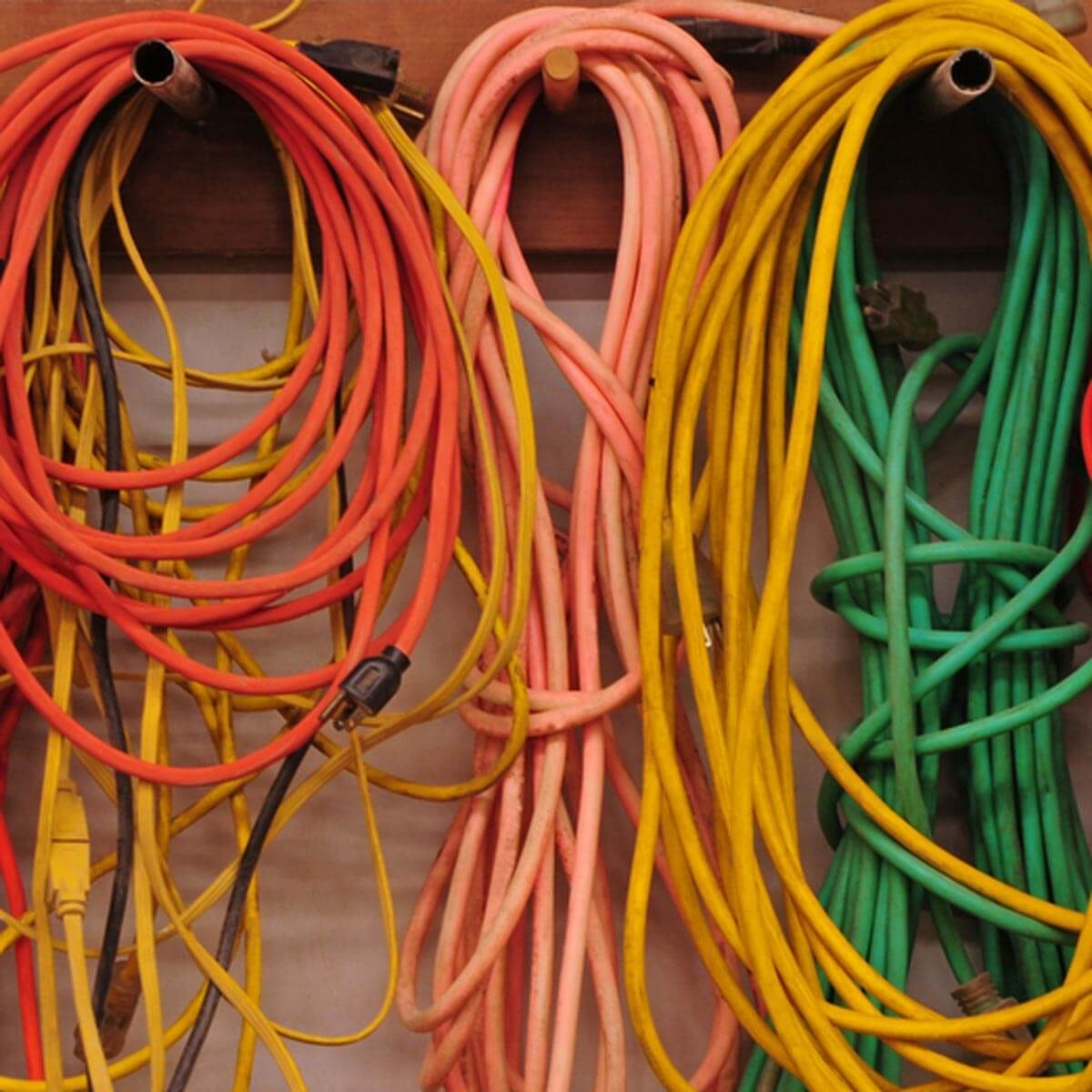Colorful extension cords hang in loops on a wooden wall, displaying various colors like red, yellow, pink, and green, suggesting organized storage.