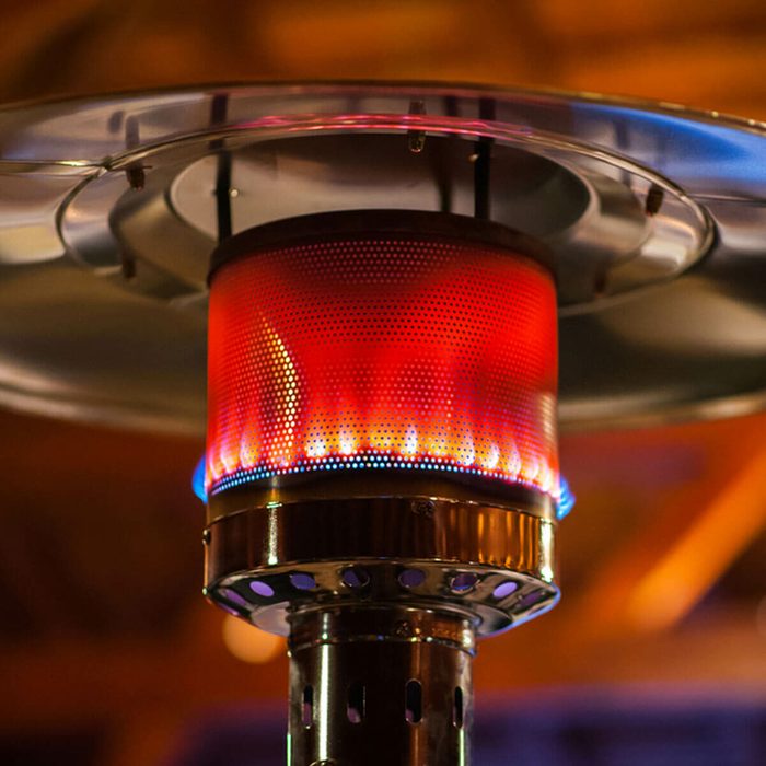 A patio heater emits bright flames from a red mesh cover, providing warmth. The setting appears dimly lit, with warm tones surrounding it.