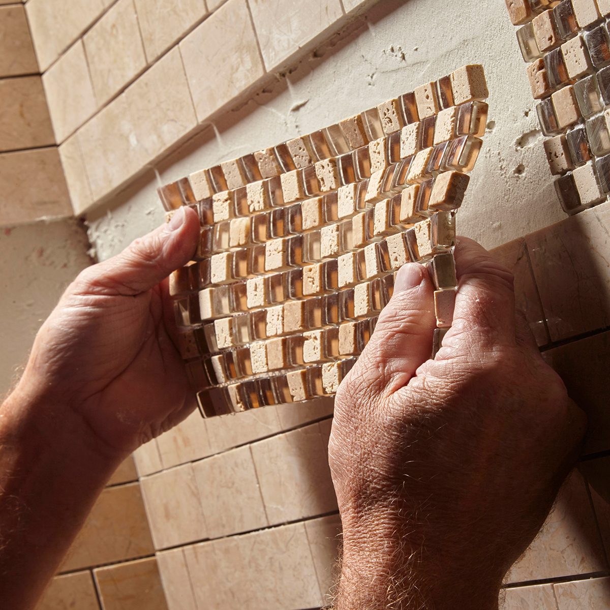 A person holds a mosaic tile sheet, preparing to apply it to a wall