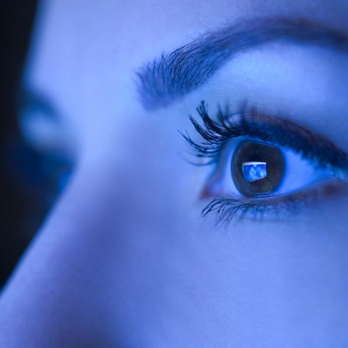 A close-up of a human eye reflects a faint blue light, suggesting focus on a nearby screen in a dimly lit environment.