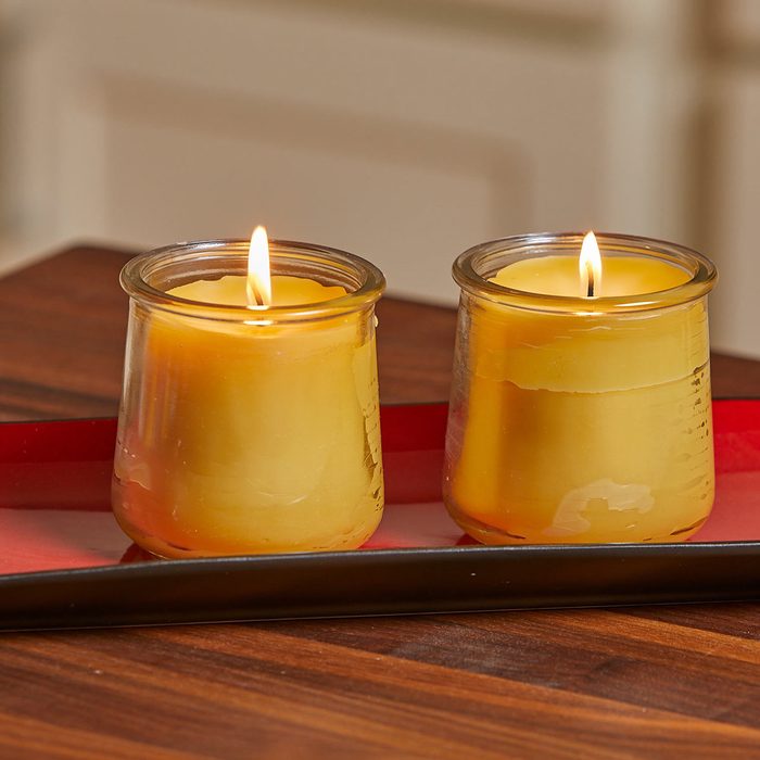 Two lit yellow candles are placed on a shallow red tray resting on a wooden surface, creating a warm, inviting atmosphere.