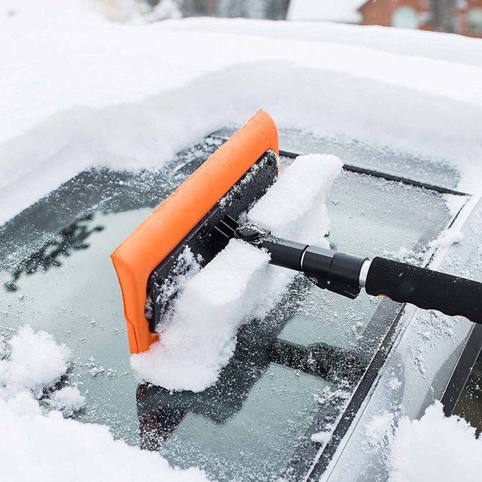 A snow brush clears a layer of snow from a car