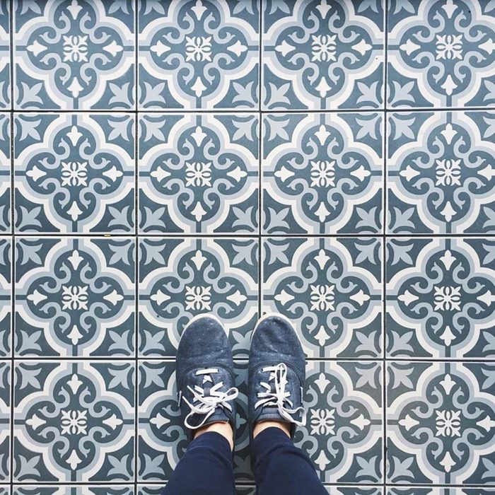 Feet wearing blue shoes stand on a patterned tile floor featuring intricate designs in shades of blue and white.