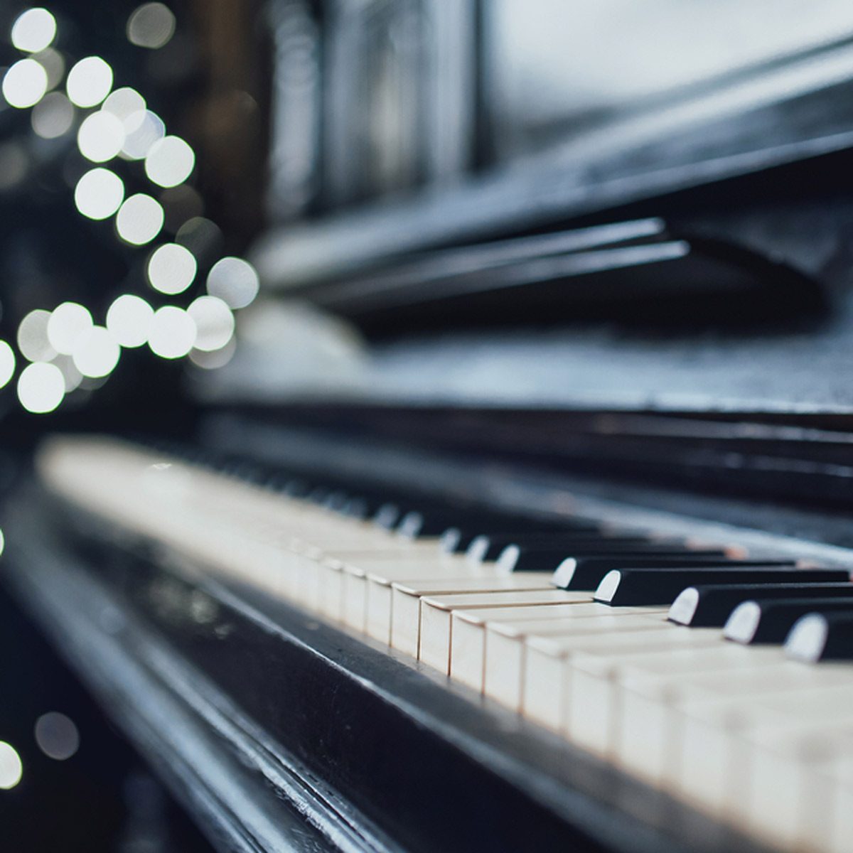A piano sits illuminated by soft, blurred lights, showcasing its keys while creating an intimate atmosphere in a dimly lit room.