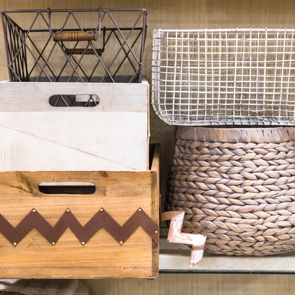 Various containers, including woven, wooden, and metal bins, are arranged on a shelf, creating an organized storage display in a neutral-toned setting.