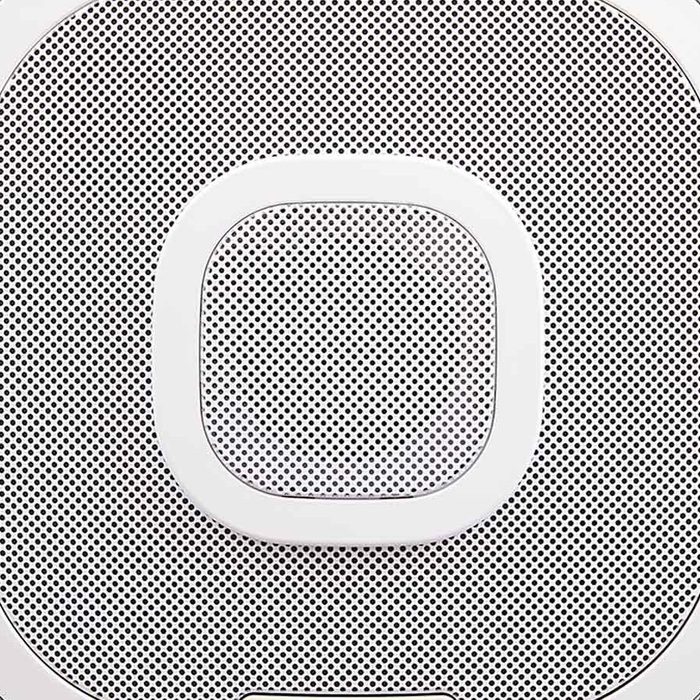 A square speaker with a mesh grille pattern sits against a neutral background, designed to emit sound and integrate into modern home environments.