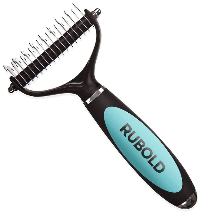 A grooming tool with a curved handle and metal prongs is positioned upright, designed for detangling and removing loose fur from animals.