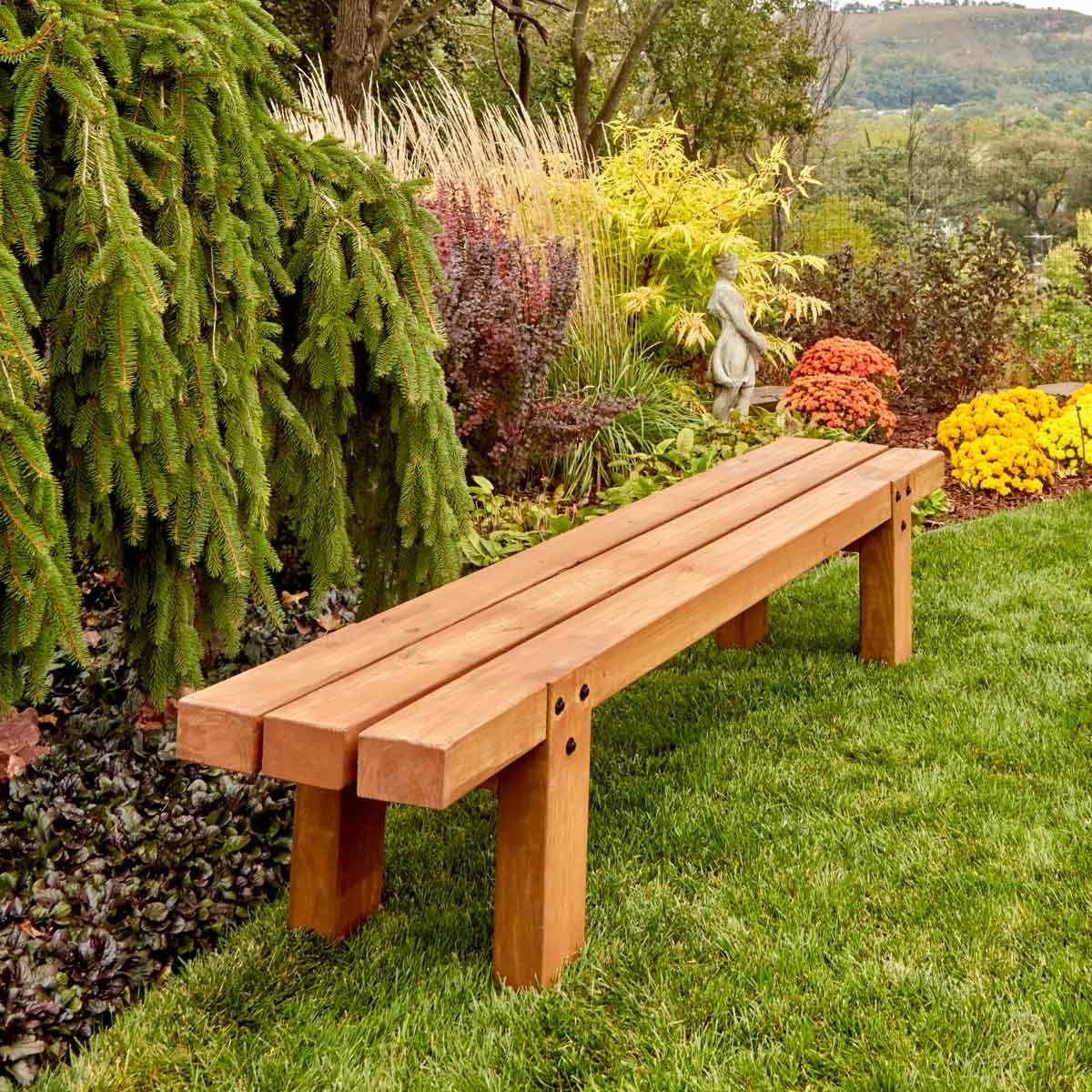 A wooden bench sits on green grass, surrounded by colorful flowers and shrubs, providing a serene spot in a landscaped garden.