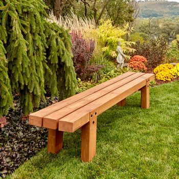 A wooden bench sits on green grass, surrounded by colorful flowers and shrubs, providing a serene spot in a landscaped garden.