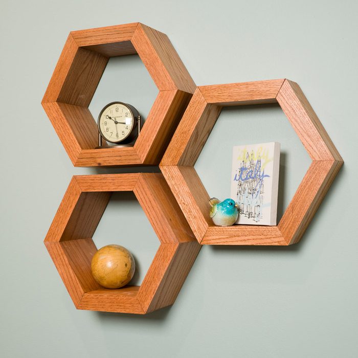 Hexagonal wooden shelves display a clock, a globe, a decorative bird, and a small artwork against a pale green wall.