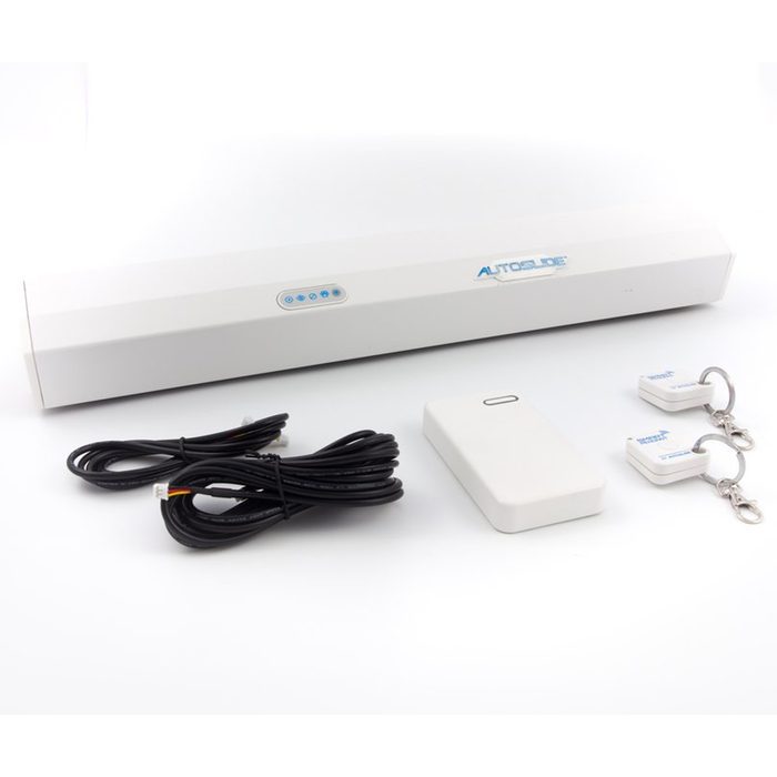 A white automatic sliding door mechanism sits on a flat surface, accompanied by two small remotes and cables, suggesting an installation for convenience.