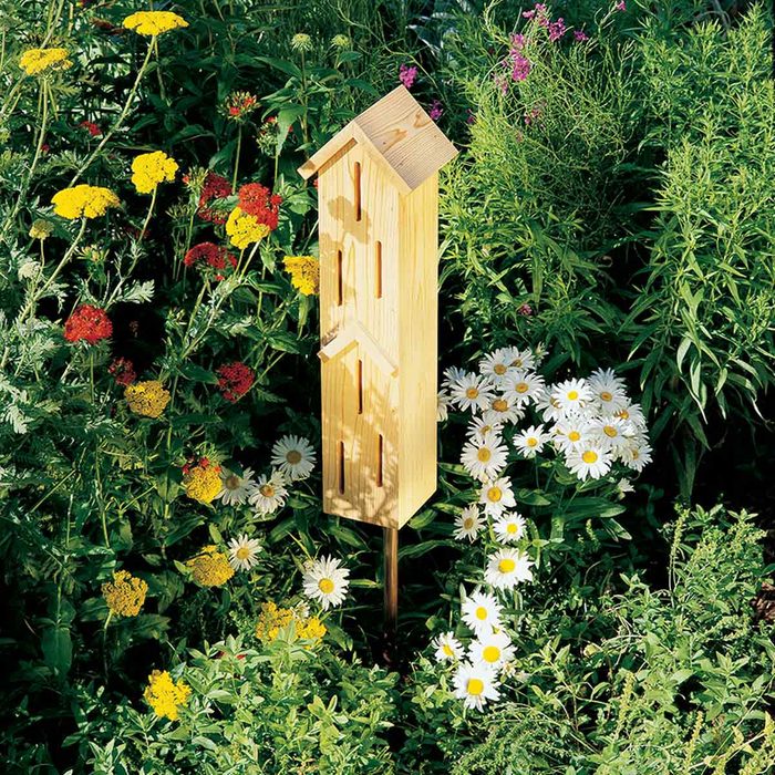 A wooden birdhouse stands upright amid vibrant wildflowers and green foliage, providing shelter in a colorful garden.