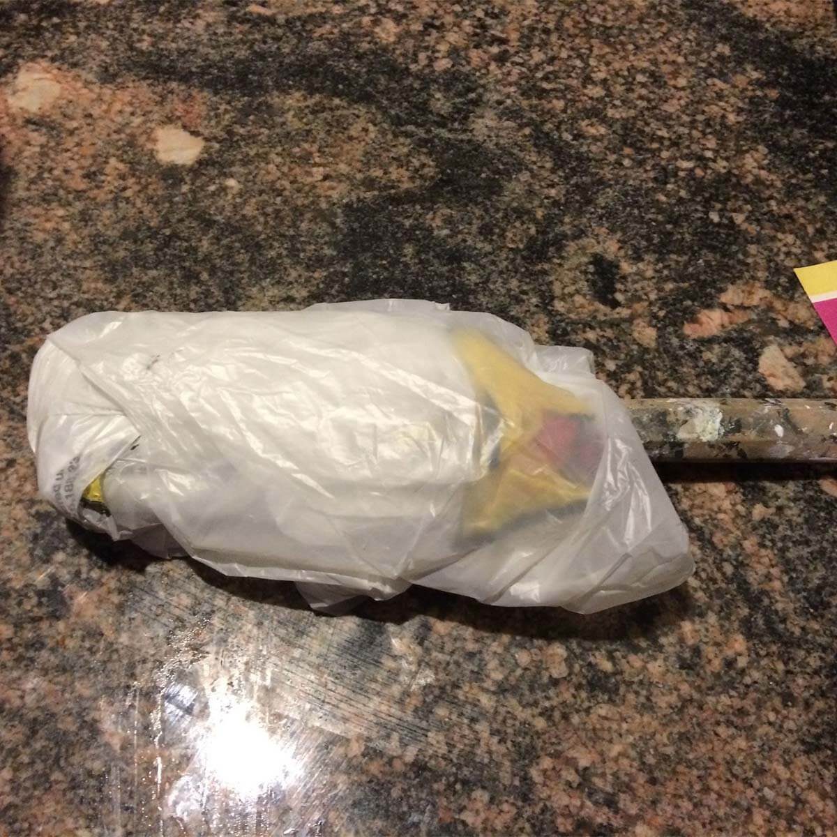 A paint roller, wrapped in a plastic bag, rests on a polished granite countertop. The surrounding surface has a speckled pattern and glossy finish.