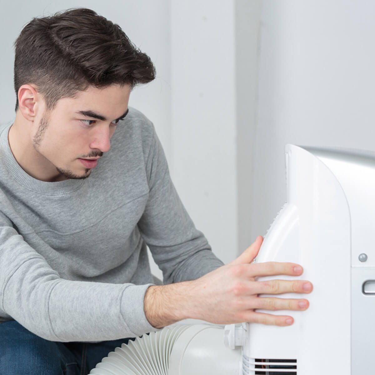 A young man inspects an appliance, focusing intently as he adjusts its settings, surrounded by a minimalistic, light-colored room.