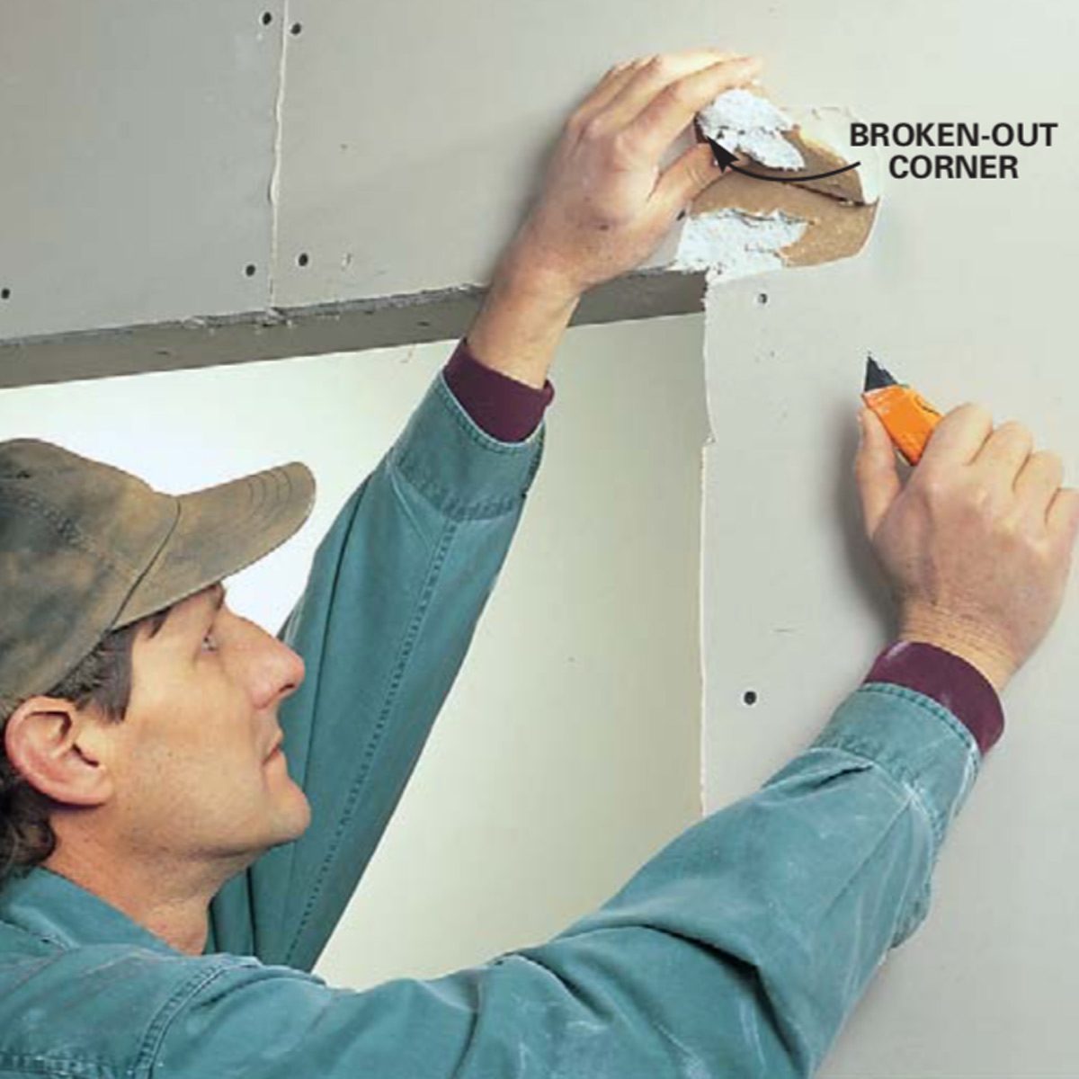 A person is repairing a broken wall corner using a utility knife, standing in an indoor setting with drywall visible around them.