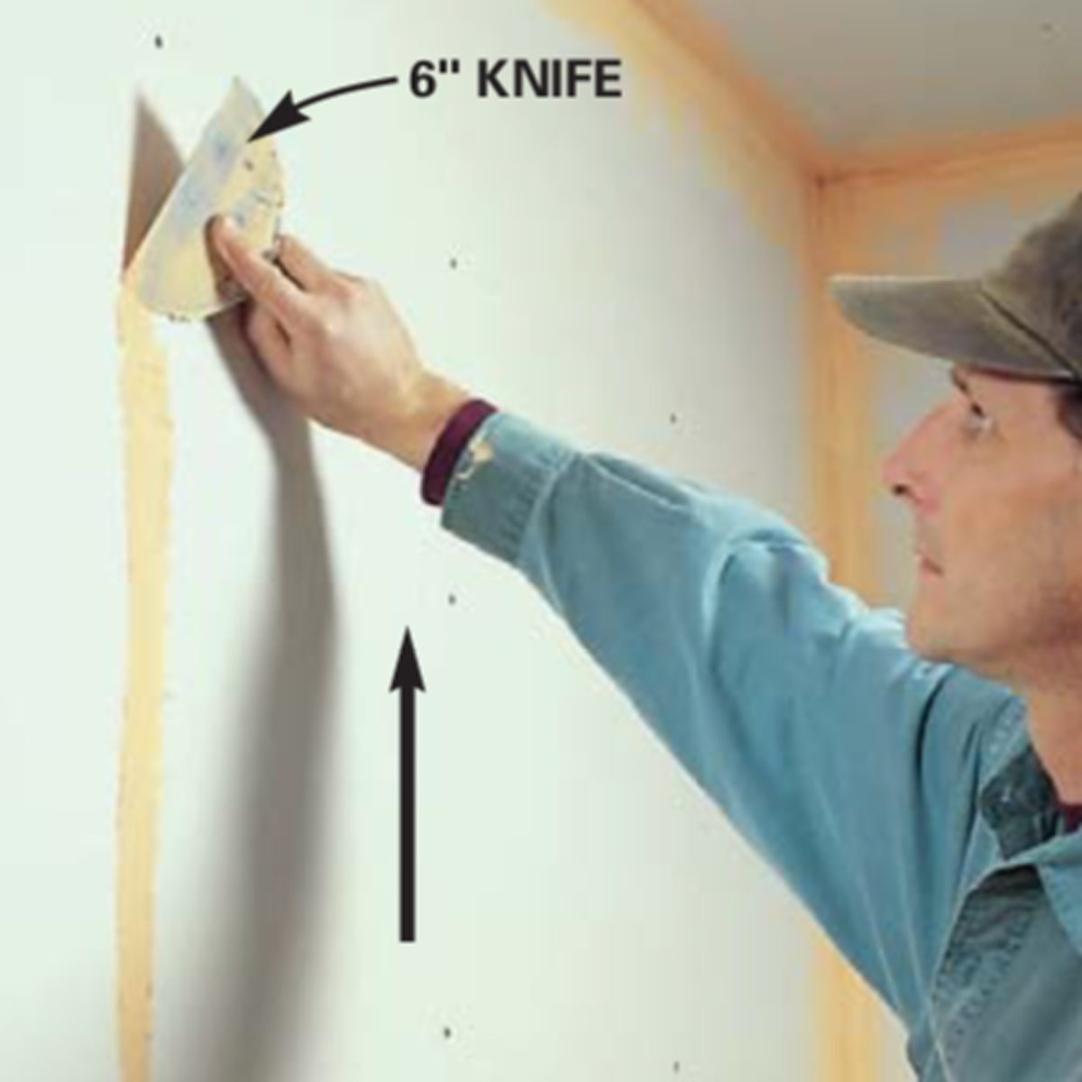 A person is applying joint compound to a wall with a 6-inch knife, focused on smoothing the surface in a construction setting.