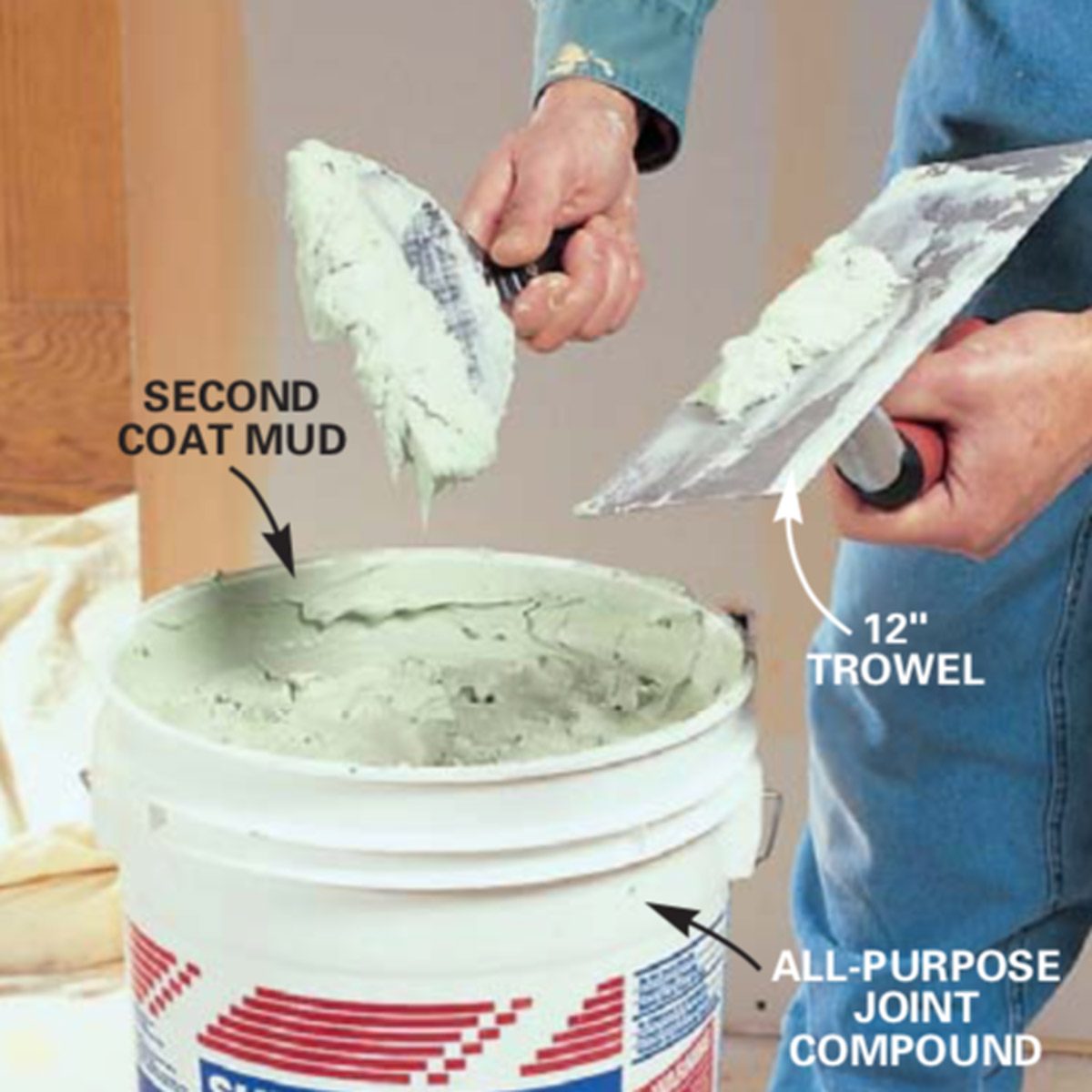 A person uses a trowel to scoop joint compound from a bucket, preparing for wall finishing in a home renovation context.
