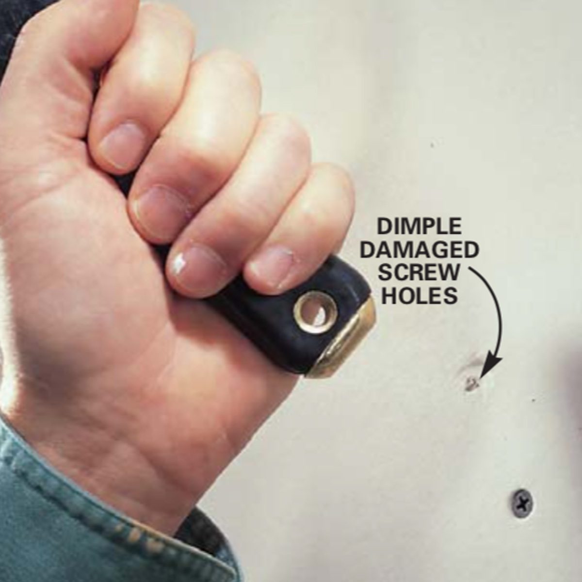 A hand holds a tool, pressing against a wall with dimpled, damaged screw holes visible nearby.