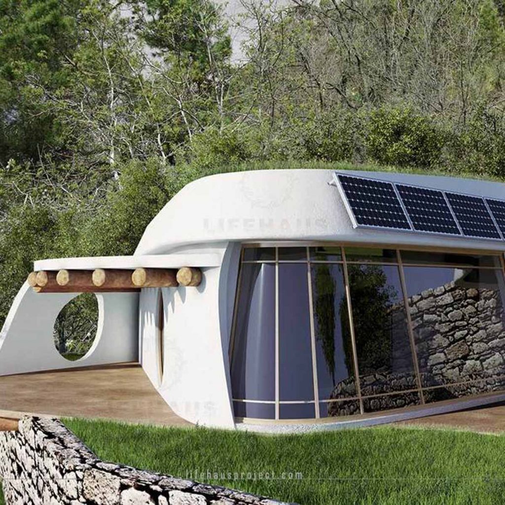 A modern, curved eco-house with solar panels sits on a green lawn, surrounded by trees, featuring large glass windows and a stone wall outside.