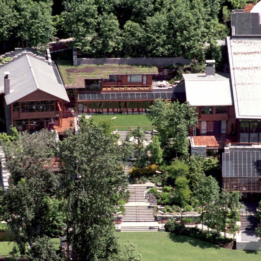 A cluster of modern buildings with green roofs sits amid lush trees, surrounded by well-maintained gardens and pathways leading through the vibrant landscape.