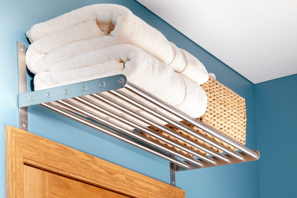 A metal shelf holds neatly stacked white towels and a woven basket above a wooden door on a blue wall, enhancing storage in the space.