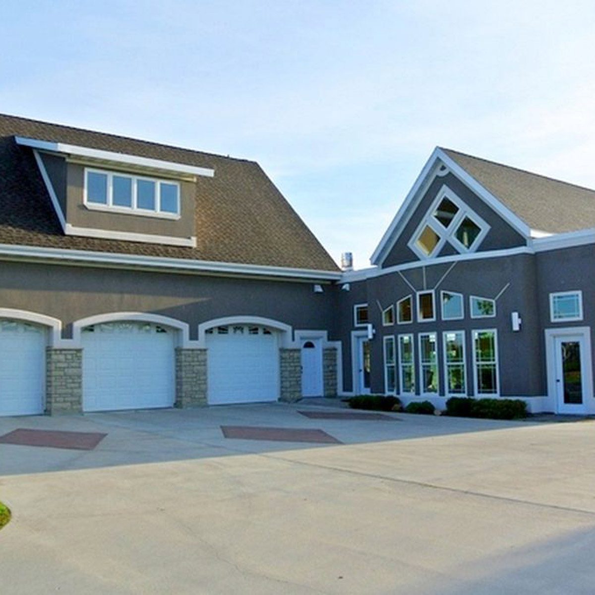 A modern house with a sloped roof showcases a mix of garage doors and large windows, situated on a paved driveway under a clear sky.
